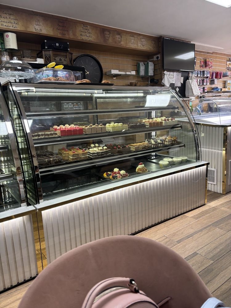 The curved glass cake cabinet filled with individual pastries, with the shop counter behind