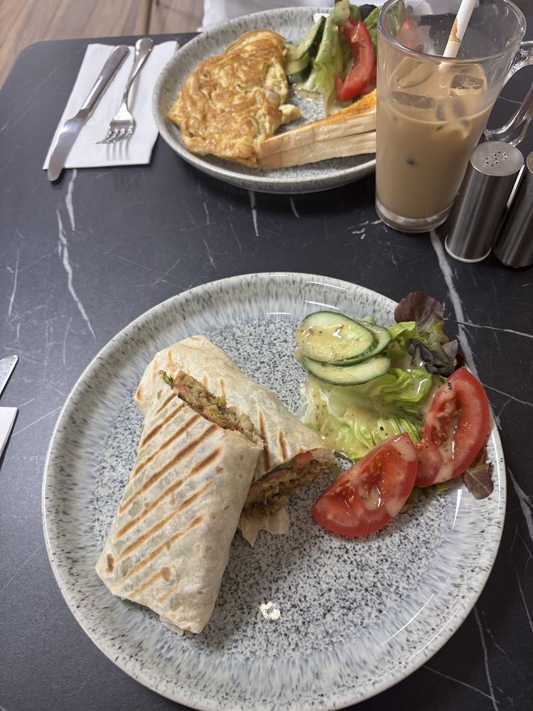 A toasted wrap with salad, an omelette dish and an iced coffee on a marble table